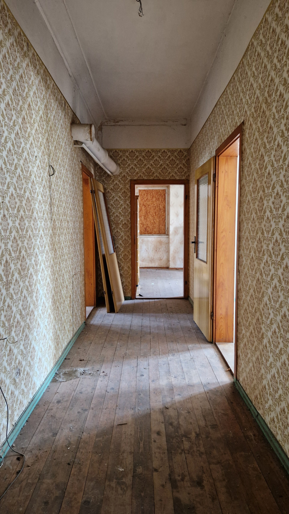 Flur in einem alten Haus. Durch eine Tür scheint Sonne auf Holzboden und Wand.